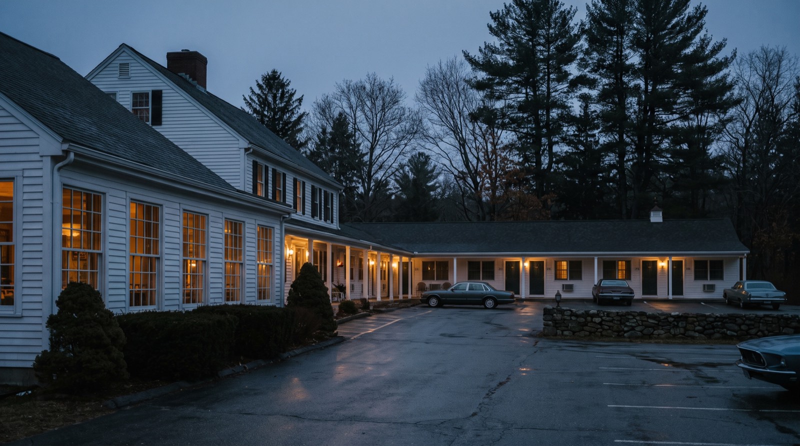 Illustrative image, not the actual property. A long white clapboard New England roadside restaurant and adjoining motor lodge wing at blue hour, warm light in the dining room windows